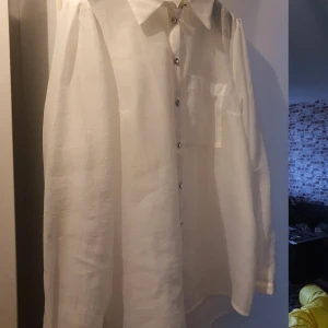 Vit linneskjorta från Pieces L - Vit skjorta i linne från Pieces i storlek L. Skjortan har långa ärmar, klassisk krage, bröstficka och snygga knappar med glittrig detalj. Perfekt för dig som gillar en clean och stilren look med en twist.