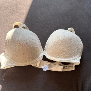 Vit spets-bh från Gina Tricot 80C - Säljer en vit bh från Gina Tricot i storlek 80C. Bh:n har vadderade kupor och är täckt med blommig spets framtill. Axelbanden är justerbara och ryggen har klassisk hyskknäppning. Använd några gångare bra skick förutom liten fläck se bild 3 