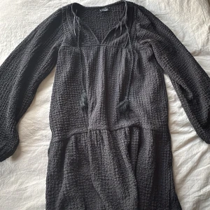 Svart långärmad klänning Gina Tricot - Svart långärmad klänning från Gina Tricot i storlek XXS. Klänningen har en strukturerad, lite krinklad yta, v-ringning med snörning och avslappnad passform.💘