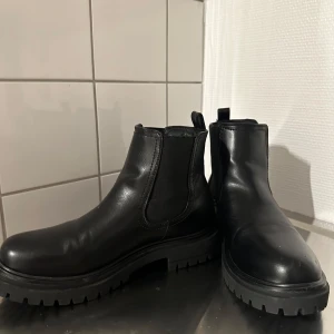 Svarta chelsea boots i skinn stl 39 - Stilrena svarta chelsea boots från North i storlek 39. Skorna är gjorda i slätt skinn med elastiska paneler på sidorna och grov sula för extra grepp. Insidan är fodrad med mjukt tyg för ökad komfort. Perfekta för höst och vinter.