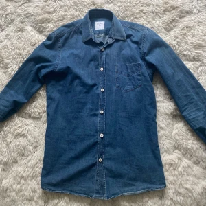 Blå jeansskjorta från Ljung - Snygg blå jeansskjorta från Ljung i storlek S. Skjortan har klassisk krage, vita knappar och en bröstficka. Perfekt till jeans eller chinos för en avslappnad look. riktigt stilren och snygg till sommaren. Frågor eller funderingar är det bara att höra av sig👍🏻