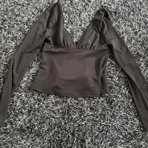 Svart omlottopp med v-ringning - Snygg svart omlottopp med djup v-ringning och långa ärmar från Nelly. Toppen har knyt i ryggen för en extra cool detalj och sitter figurnära över kroppen. Det är storlek M men den är ganska liten i storlek så skulle mer passa som S.