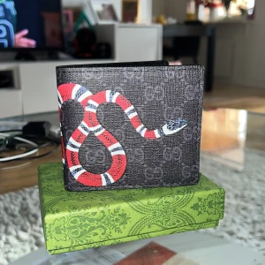 Ny plånbok med lång orm  - Snygg svart plånbok med ikoniskt GG-mönster och en  orm på utsidan. Plånboken har flera kortfack och ett fönster för ID. 