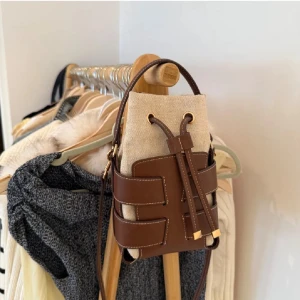 Beige och brun axelväska med snörning - Snygg axelväska i beige canvas och brunt skinn med coola detaljer. Väskan har snörning upptill, justerbar axelrem och guldfärgade metalldetaljer. Perfekt storlek för det viktigaste och ger en trendig touch till din outfit. Använd få gånger!❣️