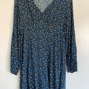 Blommig blå klänning från Clockhouse - Supersöt långärmad klänning från Clockhouse med blått och vitt blommönster. Klänningen har v-ringning och är i en flowy modell som sitter skönt. Perfekt för dig som gillar färg och mönster!