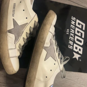 Golden Goose vita sneakers med stjärna - Golden Goose sneakers i vitt skinn med grå mockadetaljer och ikonisk stjärna på sidan. Grå snörning och silvrig häl med logga. Snygg vintage-look och platt sula.