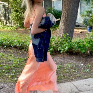 Aprikosfärgad balklänning med öppen rygg - Säljer en superfin balklänning i en unik färg, med tunna axelband och öppen rygg med knyt. Klänningen är o satin och går att justera i ryggen. Perfekt för sommarkvällar, studentfiranden eller baler!