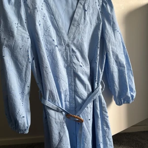 Ljusblå broderad klänning med bälte - Superfin ljusblå klänning med broderade detaljer och v-ringning. Klänningen har långa ärmar med resår vid handlederna, knappar framtill och ett matchande bälte i midjan. Perfekt för vår och sommar! Slutsåld på Zaras hemsida aldrig använd 