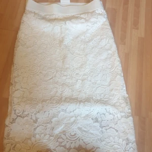 Vit spetskjol från Vila XS - Superfin vit långkjol från Vila i spets med blommigt mönster. Kjolen har en bred midjeresår och är perfekt för dig som gillar romantisk och feminin stil. Passar extra bra till vår och sommar när du vill ha något ljust och fräscht.