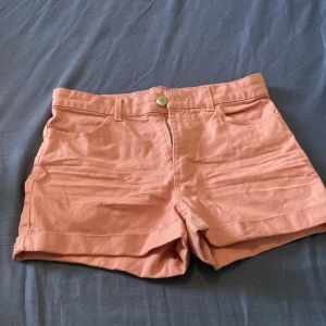 Rosa shorts från H&M, strl 152 - Snygga ljusrosa shorts från H&M i klassisk femficksmodell. De har hög midja, bälteshällor och stängs med dragkedja och knapp. Materialet är mjuk bomull med lite stretch för extra komfort. Perfekta för varma sommardagar!