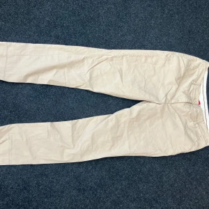 Beiga chinos från Vero Moda - Snygga beiga chinos från Vero Moda med klassisk rak passform. Byxorna har diskreta bakfickor med knapp och hällor för bälte. Perfekta för en clean och stilren look. Tillverkade i mjuk bomull för skön känsla hela dagen.
