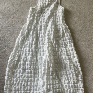 Vit långklänning från Zara med snörning - Superfin vit långklänning från Zara med coolt strukturerat tyg och smockad känsla. Klänningen har smala axelband och snygg snörning i ryggen. Perfekt för varma dagar när du vill ha något luftigt och trendigt.