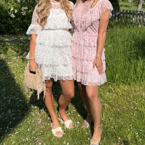 Vit spetsklänning med volanger - Superfin vit kort spetsklänning med volanger och genombrutna detaljer. Klänningen har halvlånga ärmar med volangkant, markerad midja och flera lager spets. Perfekt för somriga tillfällen och studentfirande! Använd en gång🩷