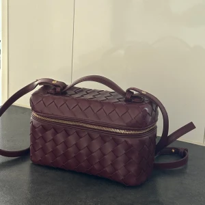 Vinröd handväska - Säljer en vinröd axelväska i flätat skinn. Perfekt storlek för det viktigaste och riktigt snygg detalj till din outfit.