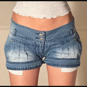 Blå jeansshorts med dubbla knappar - Snygga blå jeansshorts från Gold SK med låg midja och dubbla silverfärgade knappar framtill. Shortsen har coola sömdetaljer, fickor fram och bak samt lätt tvättad look. Storlek L men passar 36/38. 