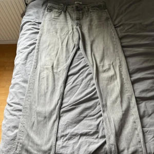 Jeans - Säljer ett par gråa jeans med rak passform och klassisk femficksdesign. Jeansen har en ljusgrå tvätt och är tillverkade i denim. Perfekta för dig som gillar en enkel och stilren look. Midjan är normal och benen är långa.