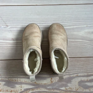 Ultra mini UGGs i färgen Sand - Beige boots från UGG i mjuk mocka med fluffigt fårfoder på insidan. Skorna har rund tå, platt sula och klassisk UGG-logga bak. Endast använd mellan 5-10 gånger!!