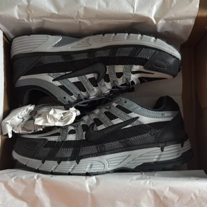 Nike p6000 - Nike p6000 sneakers i svart och grått med coola detaljer och meshpaneler för extra andningsförmåga. Skorna har snörning, platt sula och en sportig vibe. Perfekta för dig som gillar streetwear och vill ha en bekväm och snygg sneaker till vardags.