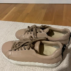 Beige sneakers från Chloé i skinn - Snygga beige sneakers från Chloé i skinn med vita vågiga sulor och bruna snören. Klassisk rund tå och svart Chloé-detalj baktill. Perfekta för dig som gillar stilrena och trendiga skor med exklusiv känsla. Sååå snygga och sitter så snyggt på foten!