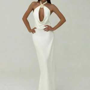 Vit långklänning med öppen rygg - Supersnygg vit långklänning med halterneck och djup urringning framtill, dekorerad med snäckdetalj vid halsen. Klänningen har öppen rygg med knyt och smal passform som framhäver figuren. 