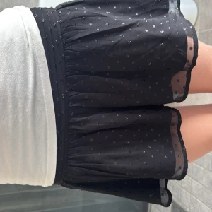 Svart kortkjol med små prickar från ginat tricot! - Supersöt svart kortkjol med små glittriga prickar och bred, rynkad midja. Kjolen är lätt och luftig med ett tunt, transparent yttertyg och volangig nederkant.🌻🌻