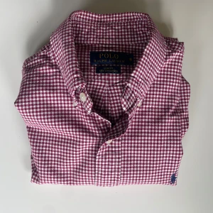 Rutig skjorta från Polo Ralph Lauren - Säljer en slim fit skjorta från Polo Ralph Lauren i rödvitt rutigt mönster. Skjortan har klassisk krage, långa ärmar och knäppning framtill. Tillverkad i bomull och har den ikoniska broderade loggan på bröstet. Säljer för 450kr