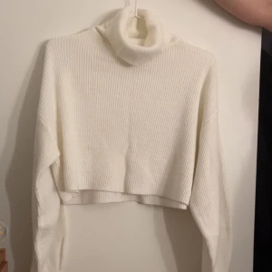 Vit croppad polotröja i ribbstickat - Superfin vit polotröja med croppad passform och ribbstickat material. Tröjan har långa ärmar och en hög polokrage som ger en stilren och trendig look. Perfekt att matcha med höga jeans eller kjol för en snygg outfit.