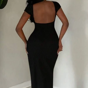 Svart långklänning med öppen rygg - Supersnygg svart långklänning med tight passform och korta ärmar. Klänningen har en djup öppen rygg som ger en riktigt elegant vibe. Perfekt för dig som vill sticka ut och känna dig extra glam. Materialet är stretchigt och följsamt.