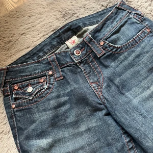 True Religion Bootcut Jeans, blå, stl 27 - Snygga blå bootcut jeans från True Religion med röda kontrastsömmar och klassiska detaljer. Jeansen är Limited edition därför de höga priset, gör ont o sälja dessa men måste tyvärr! Hoppas dessa kommer hem till någon som kommer älska de lika mycket som jag gjort :)) 