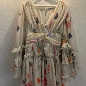 Blommig kortklänning från NA-KD - Fin sommar/midsommar klänning från Nakd x Sanna Jörnvik. Storlek 38, åt de mindre hållet. Öppen i ryggen med en knapp högst upp och dragkedja på sidan☺️Mcyket fint skick