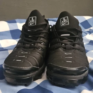Nike Air Vapormax Plus svarta sneakers - Svarta Nike Air Vapormax Plus sneakers med chunky, genomskinlig sula och snygga detaljer. Ovandel i syntet och textil, med snörning och diskreta vita accenter. Ikonisk logga på plösen och futuristisk design som sticker ut. INGEN BOX!! 