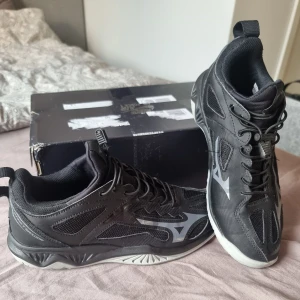 Svarta Mizuno Ghost Shadow sneakers - Svarta Mizuno Ghost Shadow sneakers med coola silvriga detaljer och logga på sidan. Ovandel i mesh och syntet för bra andningsförmåga, snörning med snabbspänne och vit sula. Perfekta för dig som gillar sportig och modern stil. OBS! Inte originell snören