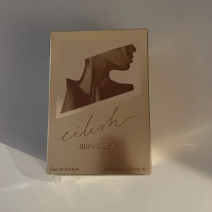 Eilish Eau de Parfum Billie Eilish - Eilish Eau de Parfum av Billie Eilish i en lyxig, guldig förpackning med en stilren siluett av en hals och ansikte. Flaskan rymmer 100 ml och designen känns modern och exklusiv, perfekt för dig som gillar trendiga dofter och snygg estetik.