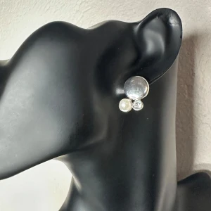 Vintageörhängen med strass & metallkula – 70/80-tal, stift, Retro - Stilfulla vintageörhängen från farmors smyckesskrin, troligen från 70-/80-talet. Tillverkade i silverfärgad metall med tre element: en kupad silverplatta, en pärla och en gnistrande strass. Stiftörhängen (ej clips), bekväma att bära. Mått ca 2,1 x 1,5 cm. Fint vintageskick med charmig patina. Prutning accepteras ej, men jag ger gärna rabatt vid köp av flera saker. Jag rensar smyckesskrin & garderob – kika gärna på mina andra annonser också!  ⸻  
