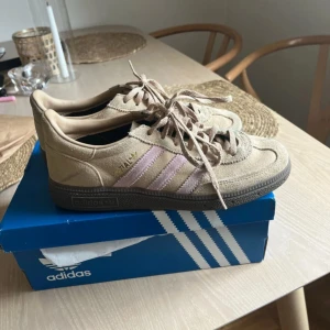 Adidas Spezial beige/rosa sneakers - Snygga Adidas Spezial sneakers i beige mocka med ljusrosa ränder och bruna sulor. Klassisk retrostil med snörning och rund tå. Perfekta för dig som gillar en clean och stilren look med en twist av färg.