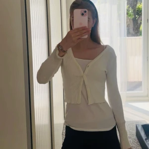 Vit ribbad kofta från Gina tricot  - Supersöt croppad kofta från Gina tricot i ribbad vit bomullsmix. V-ringad med knappar framtill och långa ärmar. Perfekt att slänga över ett linne eller en klänning. 