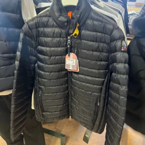 Svart pufferjacka från Parajumpers M - Säljer en svart pufferjacka från Parajumpers i storlek M. Jackan har quiltad design, hög krage och dragkedja framtill. Märkespatch på ärmen och coola detaljer som orange inslag vid kragen. Perfekt för kalla dagar och riktigt snygg streetstil.