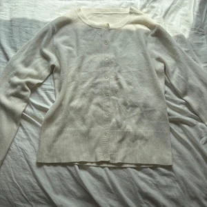 Vit kofta med knappar - Klassisk vit kofta med rund halsringning och knäppning framtill. Långa ärmar och ribbade muddar ger en clean och stilren look. Perfekt att slänga över en t-shirt eller klänning för en chill vibe. Jättemjuk och skön! Står ingen storlek eller märke.