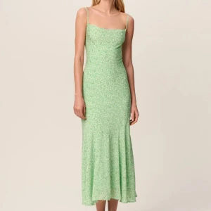 Ny adoore klänning - Superfin långklänning i ljusgrönt med små vita blommor. Klänningen har smala axelband, öppen rygg med snörning och en lätt utsvängd siluett. Perfekt för sommarens alla tillfällen. Prislapp finns kvar