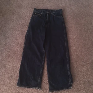 Sweet SKTBS wide jeans med brodyr - Mörkblå jeans från Sweet SKTBS med bred passform och råa, fransiga benslut. Baksidan har stora fickor och gul brodyr med texten 'Sweet SKTBS'. Klassisk femficksmodell i robust denim, perfekt för en streetwear-look.