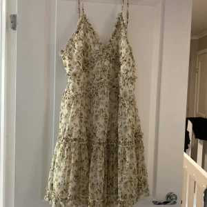 Blommig volangklänning med smala axelband - Supersöt kort blommig klänning med volanger och smala axelband. Klänningen är vit med ljusgula och gröna blommor, har v-ringning och flera volangdetaljer. Perfekt för sommarens alla tillfällen och ger en romantisk vibe. storlek 40 men passar mig som är M