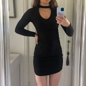 Svart ribbad kortklänning med cut out - Snygg svart ribbad kortklänning med lång ärm och cut out-detalj vid halsen. Knappt använd💕