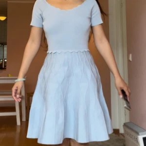 Ljusblå kortklänning från Sandro  - Supersöt ljusblå kortklänning från Sandro Paris med vågig kant vid midjan och halsringning. Klänningen har korta ärmar och ett subtilt mönster på kjolen. Materialet är mjukt och stretchigt, perfekt för vår och sommar. Enkel men ändå unik design som känns fräsch och trendig.