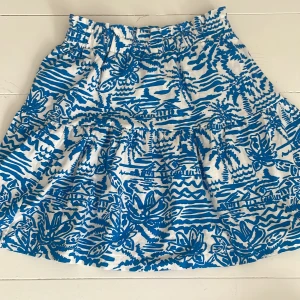 Vit och blå mönstrad kjol från Zara - Superfin kort kjol från Zara med elastisk midja och fint blått mönster på vitt. Kjolen har volang och är perfekt för sommaren. Lätt och luftig i bomull, mjuk och skön att ha på sig.