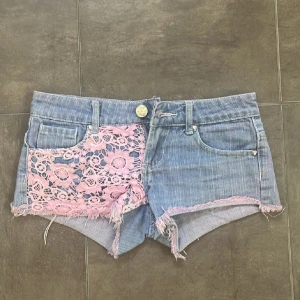 Blåa lågmidjade jeansshorts - Snygga blå lågmidjade jeansshorts med rosa spetsdetaljer. Små jättesöta hjärtformade metalldetaljer vid fickorn. Perfekta för sommaren!!! Hör av er via frågor eller funderingar! OBBSSS!! Sålde ett par exakt likadana, så bli inte förvirrade. Midjemåttet är 37,5 cm💗