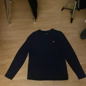 Mörkblå långärmad tröja Lyle & Scott - Snygg mörkblå långärmad tröja från Lyle & Scott med klassisk gul logga på bröstet. Tillverkad i 100% bomull, perfekt för dig som gillar stilrena och enkla plagg. Passar lika bra till jeans som till chinos.