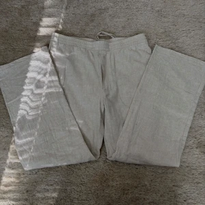Beiga linnebyxor från H&M - Säljer ett par beiga linnebyxor från H&M med dragsko i midjan. Byxorna har raka ben och avslappnad passform, perfekta för varma dagar. Materialet är svalt och luftigt linne.