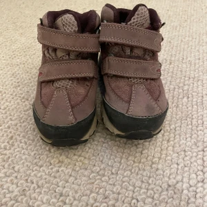 Bruna barnboots från Timberland - Säljer ett par brun/lila boots för barn från Timberland med två kardborreband och robust sula. Skorna har detaljer i mocka och mesh samt förstärkt tå och häl. Perfekta för utomhuslek under höst och vinter. Skona är också goretex.