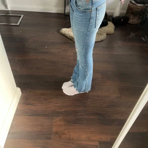 Blå bootcut jeans med slitningar - Säljer ett par blå bootcut jeans med slitningar på båda benen och råa kanter nertill. Inga defekter, alla hål fanns sen innan.