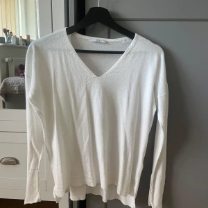 Vit v-ringad stickad tröja - Säljer en stilren vit stickad tröja med v-ringning och långa ärmar. Tröjan har ribbade muddar vid ärmslut och nederkant, vilket ger en snygg detalj. Perfekt att matcha med jeans eller kjol.